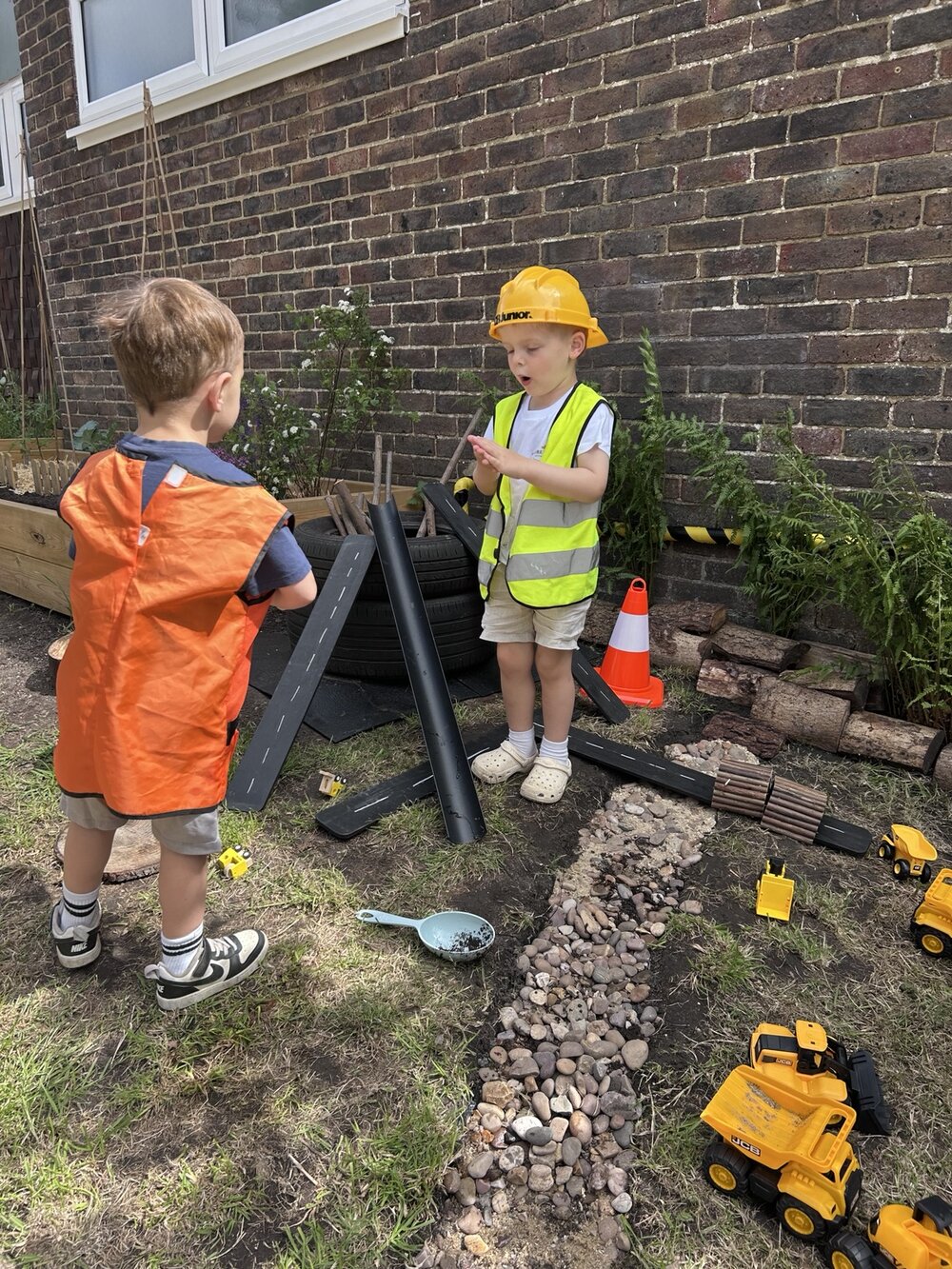 Children using toy trucks, ramps and dressing-up clothes outside
