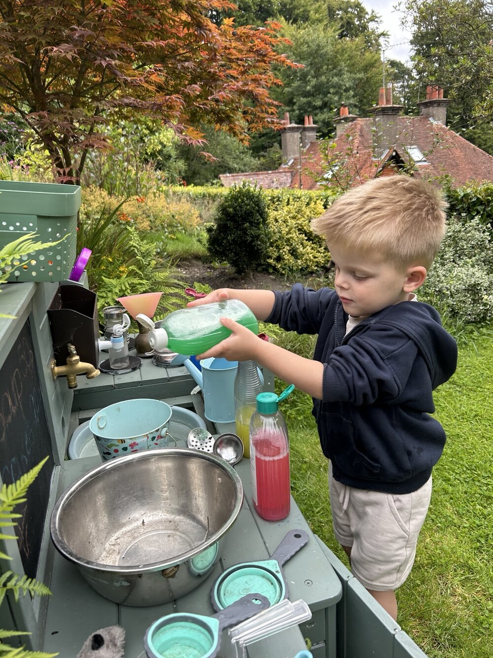 A child pouring at an outdoor mud kitchen